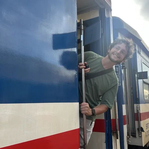 Quentin asomado a la puerta de un tren, sonriendo